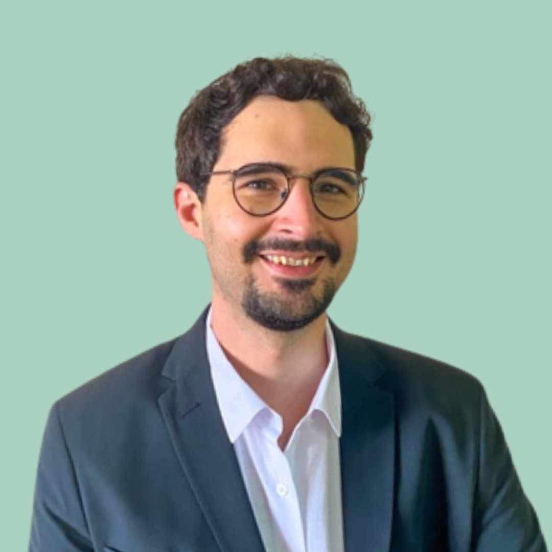 Foto de Pedro Forti, com cabelos curtos e escuros, sorrindo e olhando diretamente para a câmera.